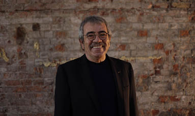 Selçuk Yöntem smiling in front of a brick wall